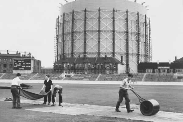 With the landmark gasometer forming the backdrop groundsmen work to roll and cover the wicket in preparation for the Surrey County Cricket Club v The Rest of England match on 7 September 1956 at the Kennington Oval cricket ground in London, United Kingdom.  (Photo by Central Press/Hulton Archive/Getty Images).