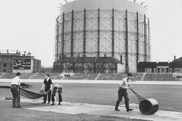 With the landmark gasometer forming the backdrop groundsmen work to roll and cover the wicket in preparation for the Surrey County Cricket Club v The Rest of England match on 7 September 1956 at the Kennington Oval cricket ground in London, United Kingdom.  (Photo by Central Press/Hulton Archive/Getty Images).
